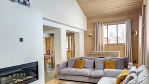 Ein modernes Wohnzimmer mit Kamin, grauem Sofagarnitur und Holzbalkendecke.
