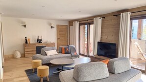 Ein modernes Wohnzimmer mit einem grauen Sofa, einem runden Couchtisch und einem Fernseher. Es gibt ein Holzregal und einen Kamin.