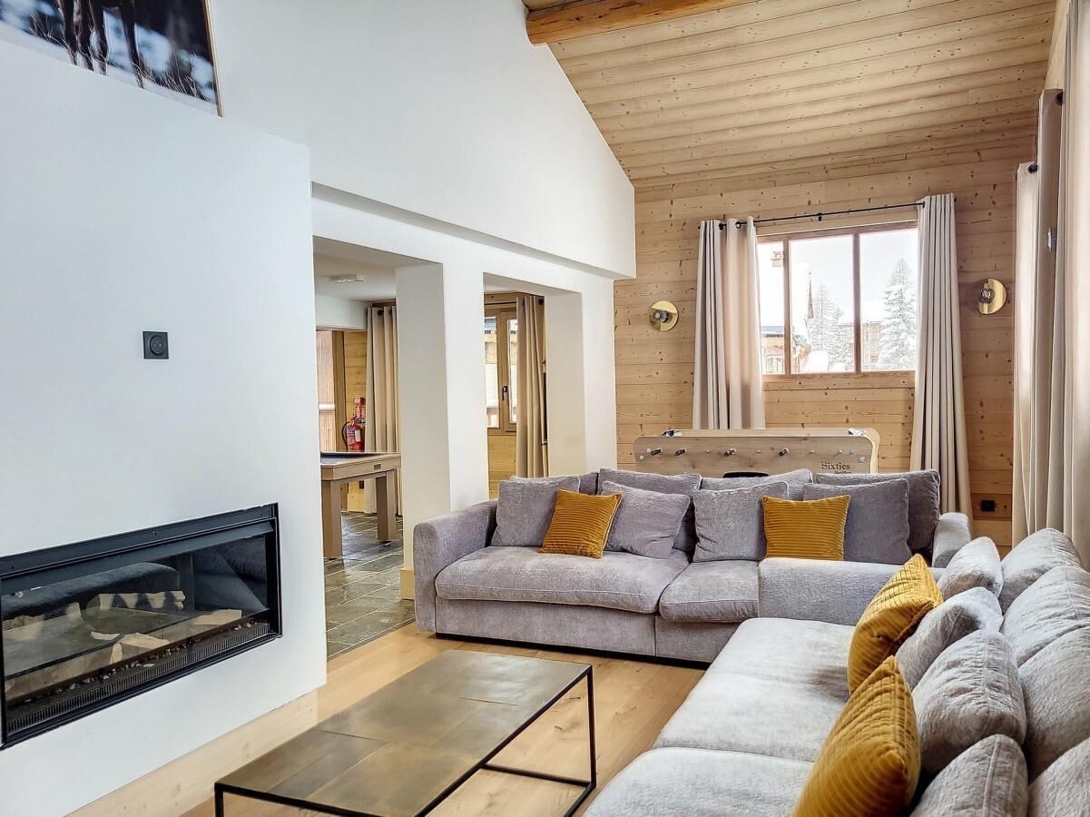 Ein modernes Wohnzimmer mit Kamin, grauem Sofagarnitur und Holzbalkendecke.
