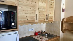 A kitchen with wooden cabinets, a microwave, a refrigerator, a sink, and a patterned mat on the countertop. - 100m from resort center, 2nd floor, balcony, tv, ski locker, 40m², Serre Chevalier (La Salle-les-Alpes)