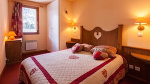 A cozy bedroom with a large bed, two bedside lamps, a window with curtains, and a radiator. - 100m from resort center, 2nd floor, balcony, tv, ski locker, 40m², Serre Chevalier (La Salle-les-Alpes)