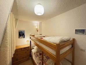 A bunk bed room with a wooden headboard, a bedside table with a lamp, and a wall-mounted light fixture.