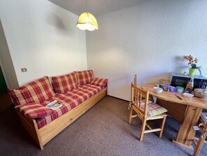 A small room with a wooden sofa, a dining table with chairs, a lamp, and a microwave.