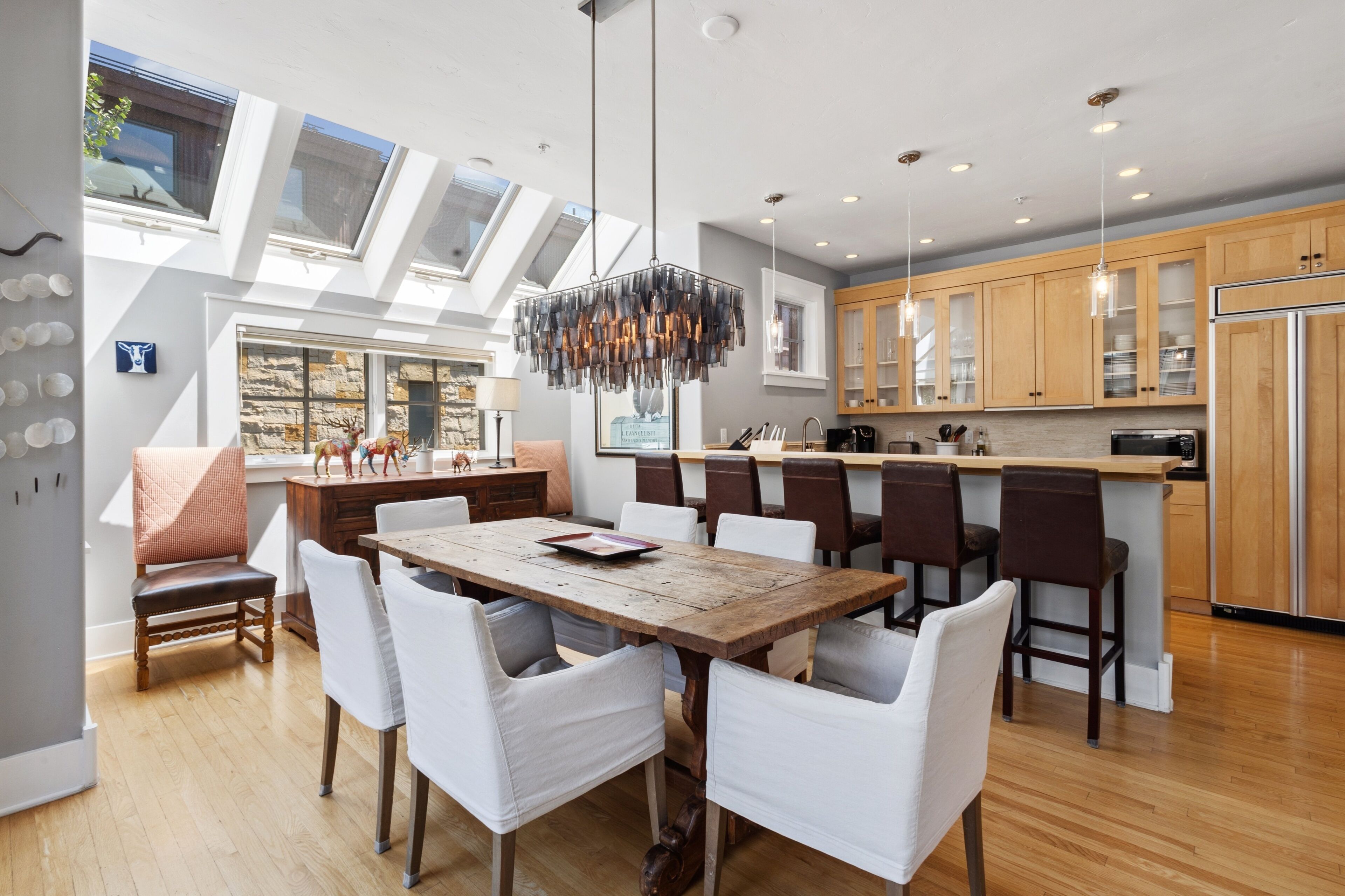 A modern kitchen with wooden cabinets, a central island, and a dining area with a wooden table and white chairs.