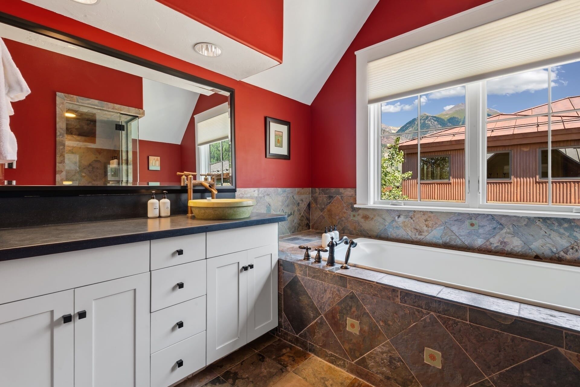 A bathroom with a large mirror, a bathtub, and a window with a view of a mountain.