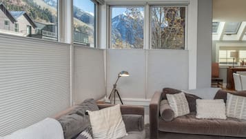 A modern living room with large windows, a sofa set, and a lamp.
