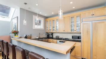 A modern kitchen with a central island, wooden cabinets, stainless steel appliances, and pendant lighting.