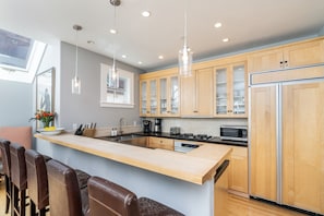 A modern kitchen with a central island, wooden cabinets, stainless steel appliances, and pendant lighting.