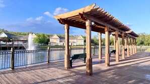 A wooden deck with a pergola, benches, and a view of a body of water and houses.