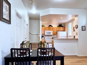 A dining area with a table and chairs, a kitchen with wooden cabinets and appliances, and a hallway with white walls and a door. - Lovely Family Townhome In Great Location-2200scd 4 Bedroom Townhouse by RedAwning (Kissimmee)