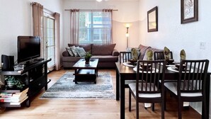A living room with a TV, sofa, coffee table, and dining area with chairs and a table.