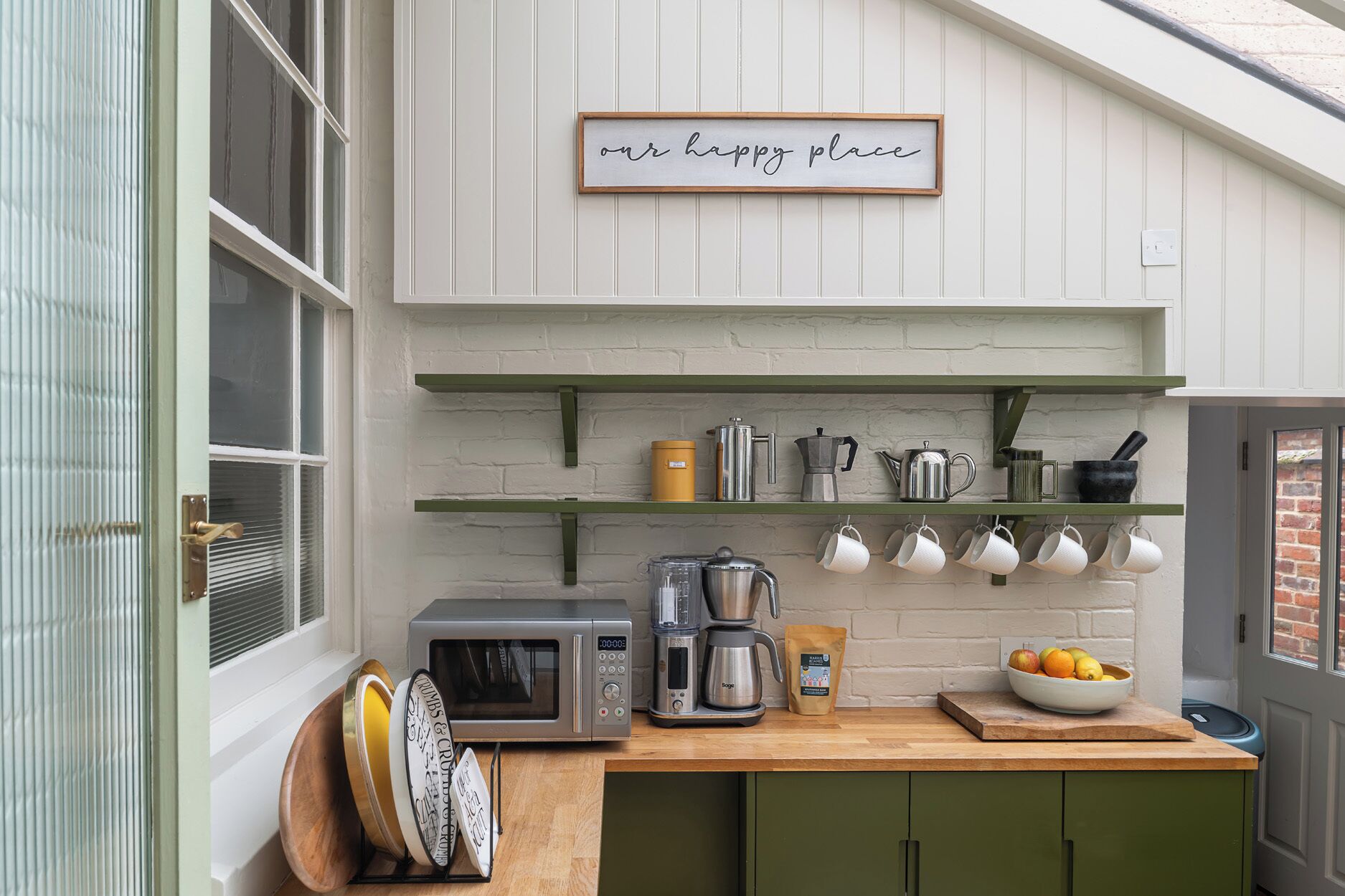 Una cocina con cafetera, tostadora y un bol de fruta en la encimera.