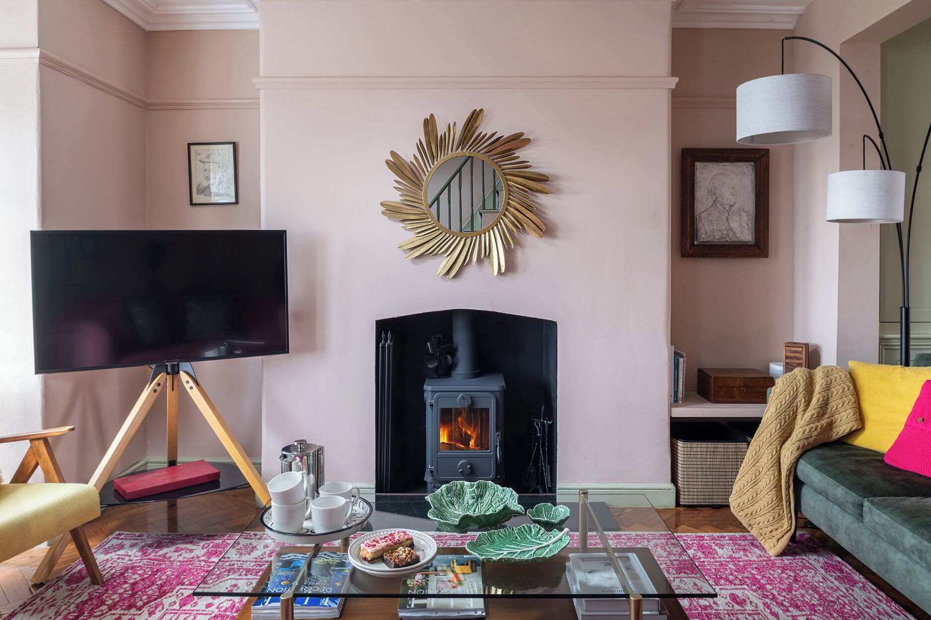 A living room with a fireplace, a television, and a coffee table with magazines and a plate of food.