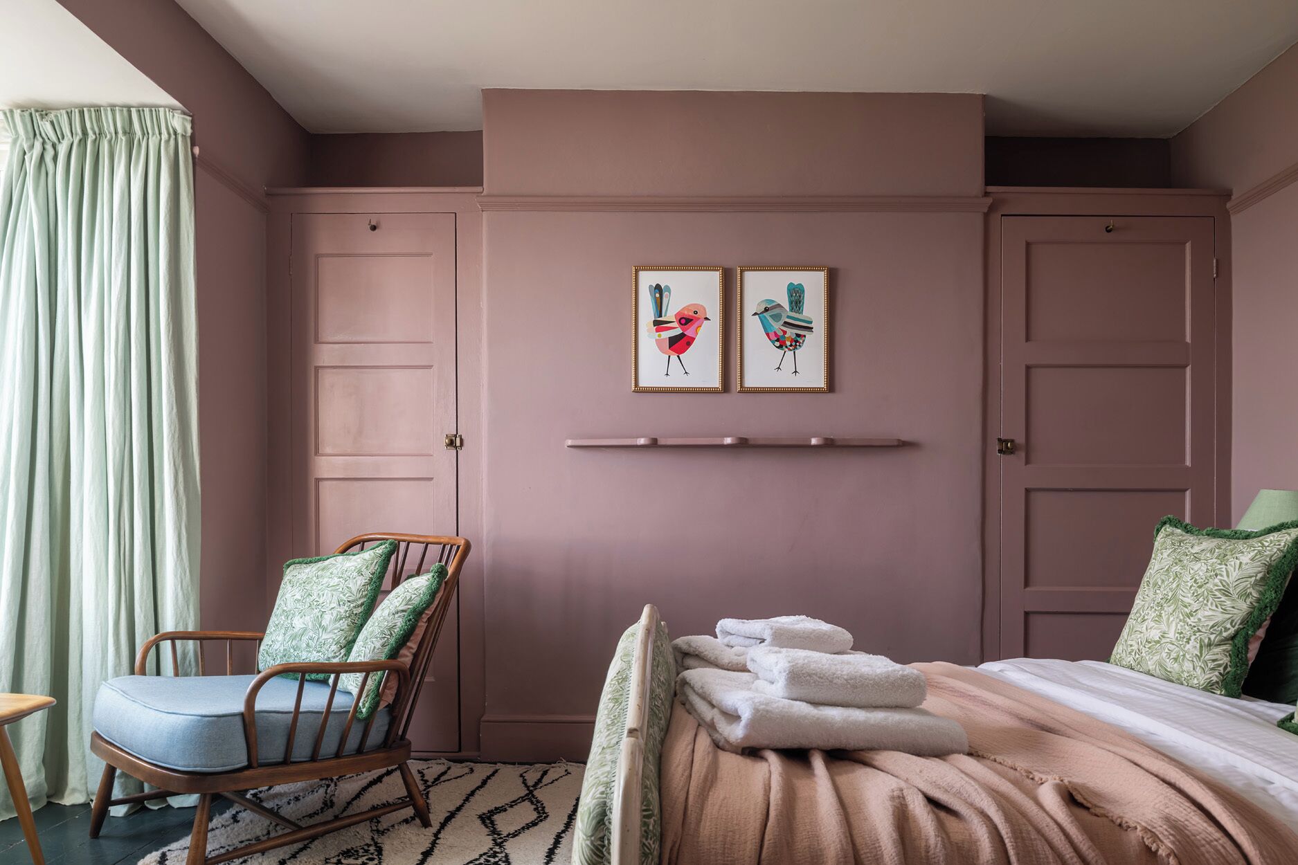 A bedroom with a bed, a chair, a window with curtains, and two wall-mounted pictures.