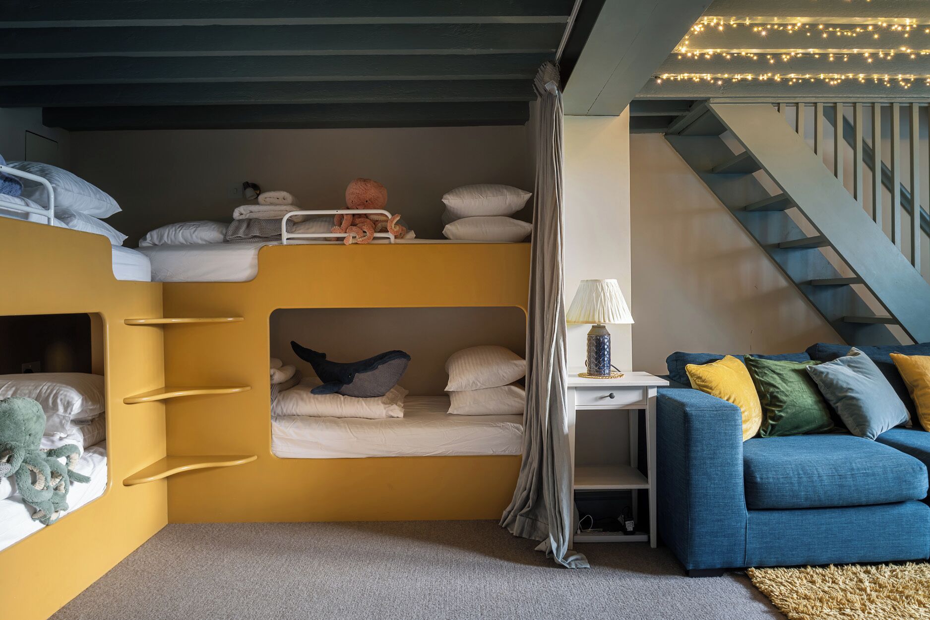 Een kleine kamer met stapelbedden, een bureau, een lamp en een blauwe bank.