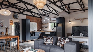 A modern interior with exposed beams, a kitchen, a sofa with patterned cushions, and a dining area. - Grace of Africa (Nkomazi)