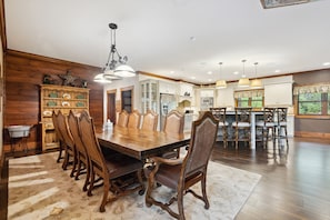 A spacious dining area with a large wooden table and matching chairs, a chandelier, and a view of the kitchen in the background. - Luxury Lodge Sleeps 26 Comfortably at Sapphire Valley Resort (Sapphire)