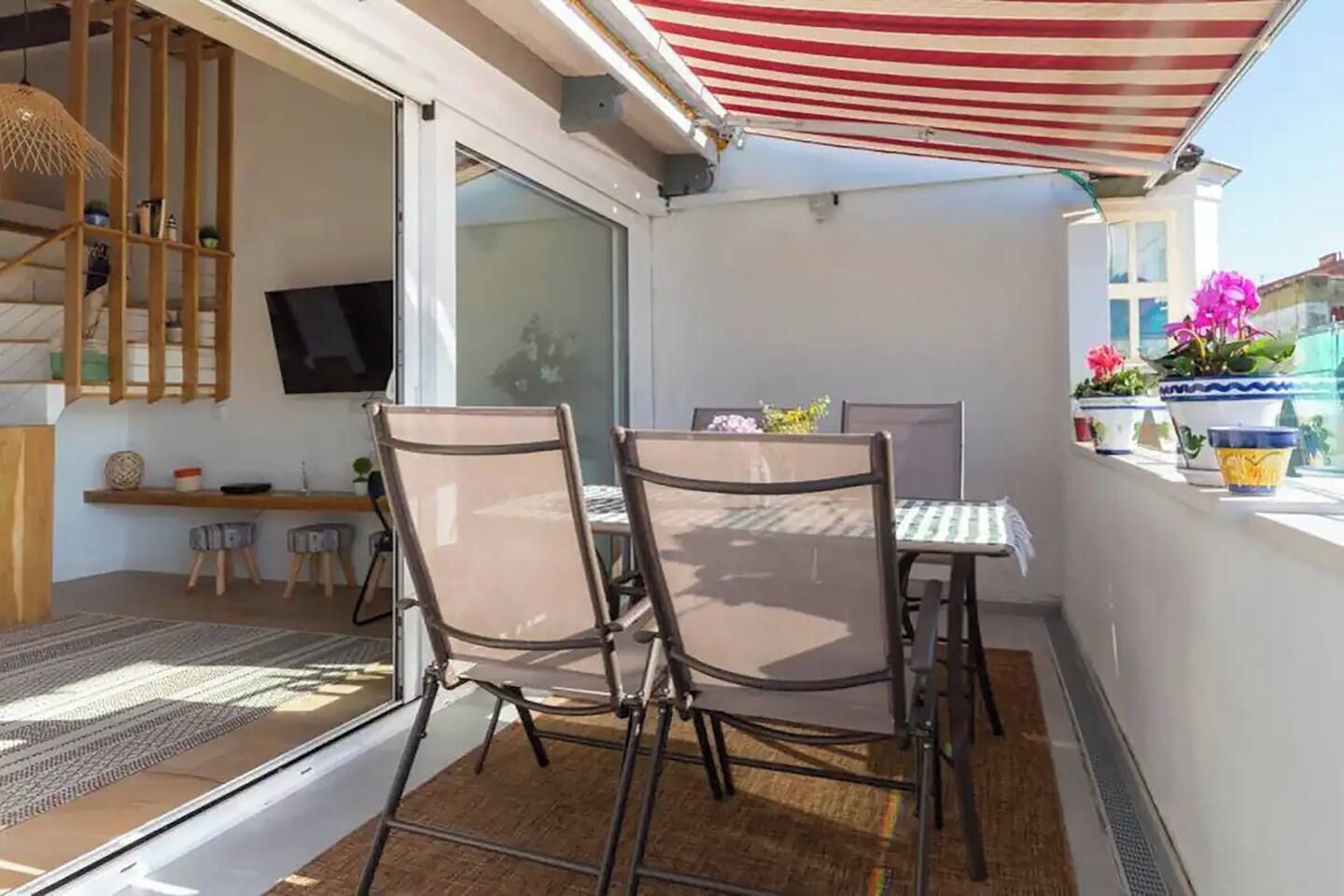En balkon med et bord og stole, et fjernsyn ophængt på væggen og plantekasser.