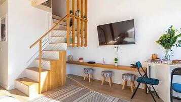 Un espacio habitable moderno con una escalera de madera, un televisor de pantalla plana montado en la pared, una zona de bar con taburetes y una mesa de comedor.