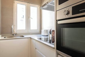 Een keuken met een inbouwoven, een spoelbak van roestvrij staal en een raam boven de spoelbak.