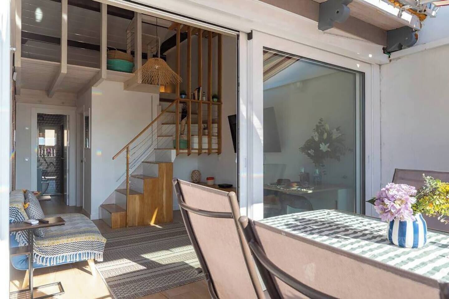 Un interior moderno con una escalera, una zona de comedor con mesa y sillas, y un ventanal grande.