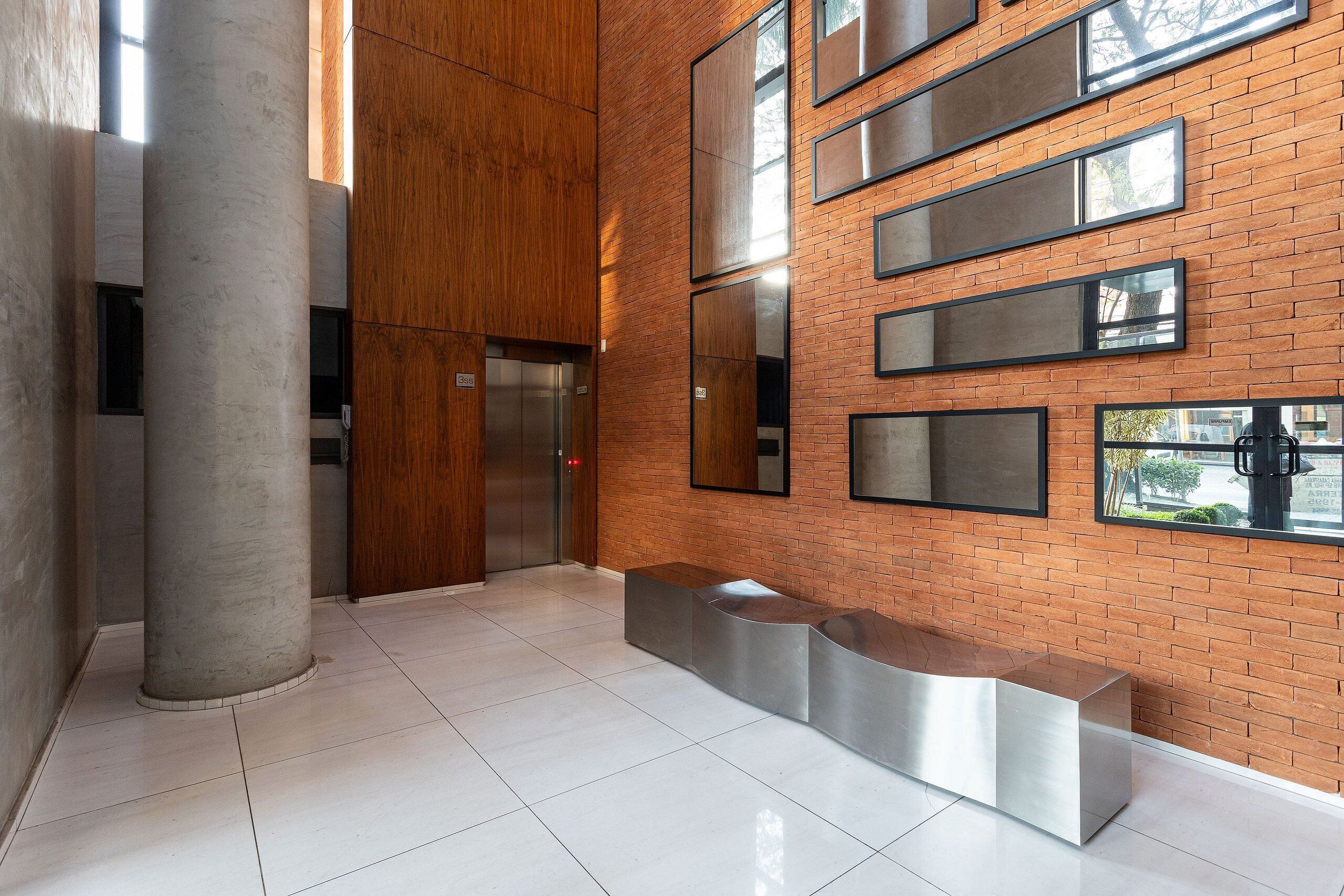 A lobby with a modern design, featuring a brick wall, large windows, and a reception desk.