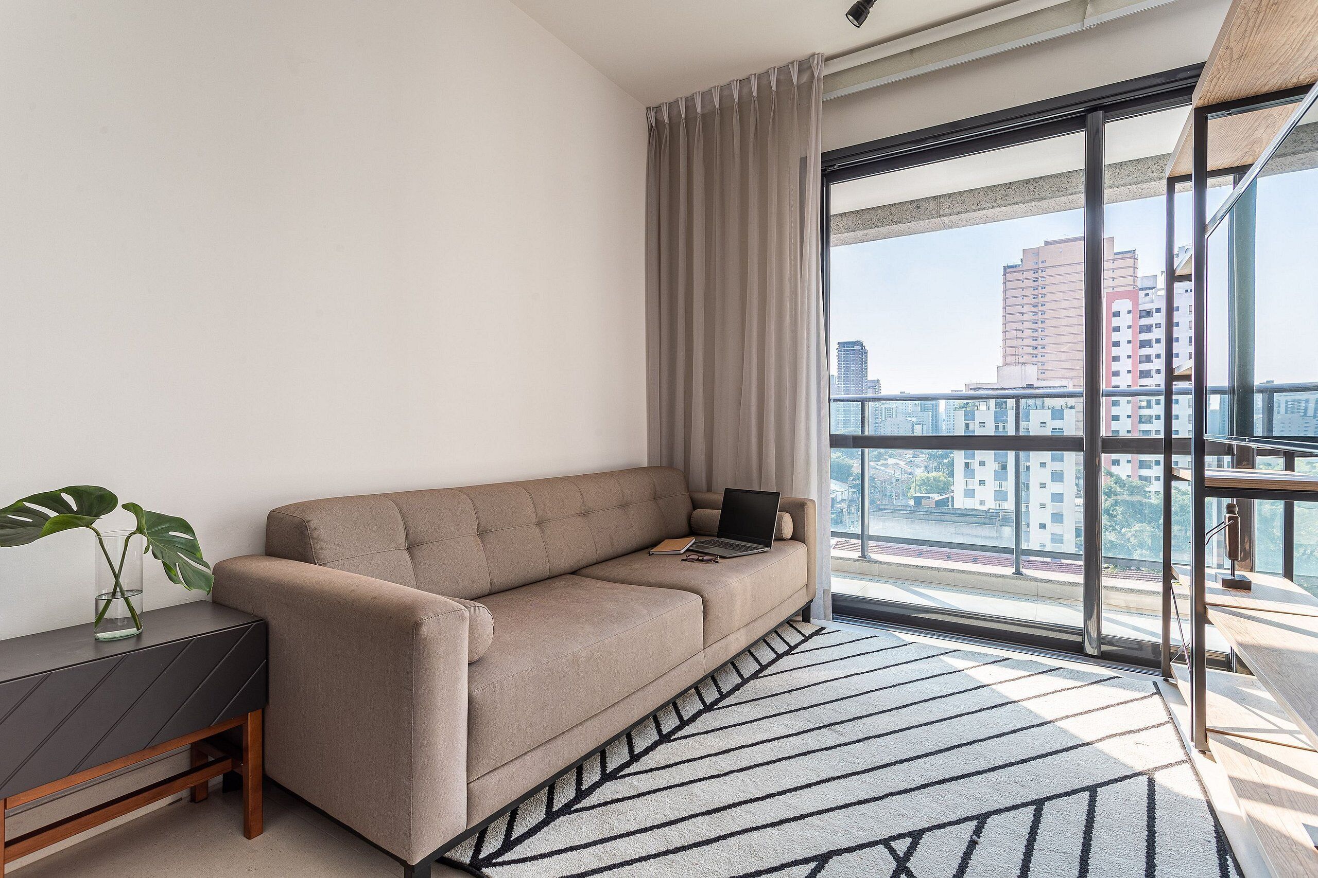 A modern living room with a sofa, a glass coffee table, and a view of the city through large windows.