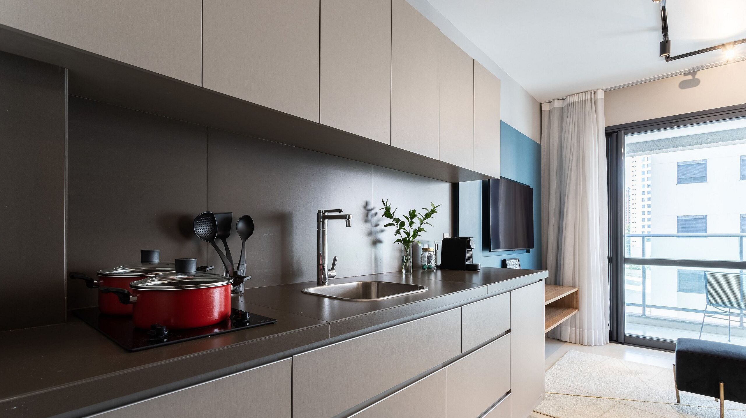 A modern kitchen with a built-in stove, a sink, and a flat-screen TV mounted above it.