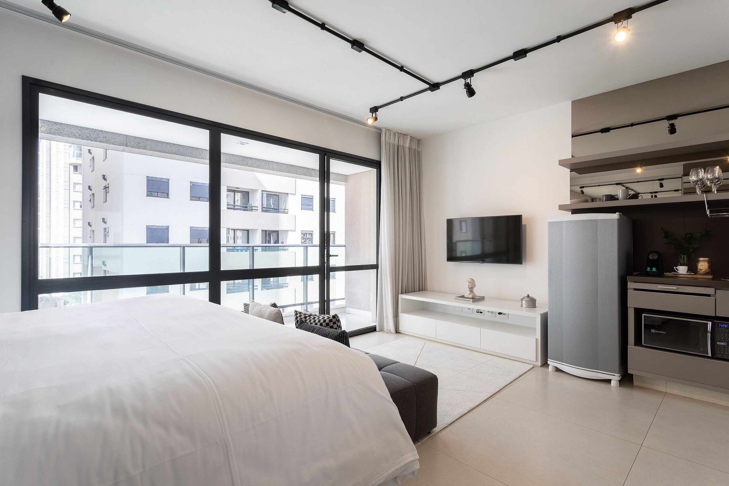 Een moderne hotelkamer met een groot bed, een kitchenette, een televisie en een balkon met uitzicht op de stad.