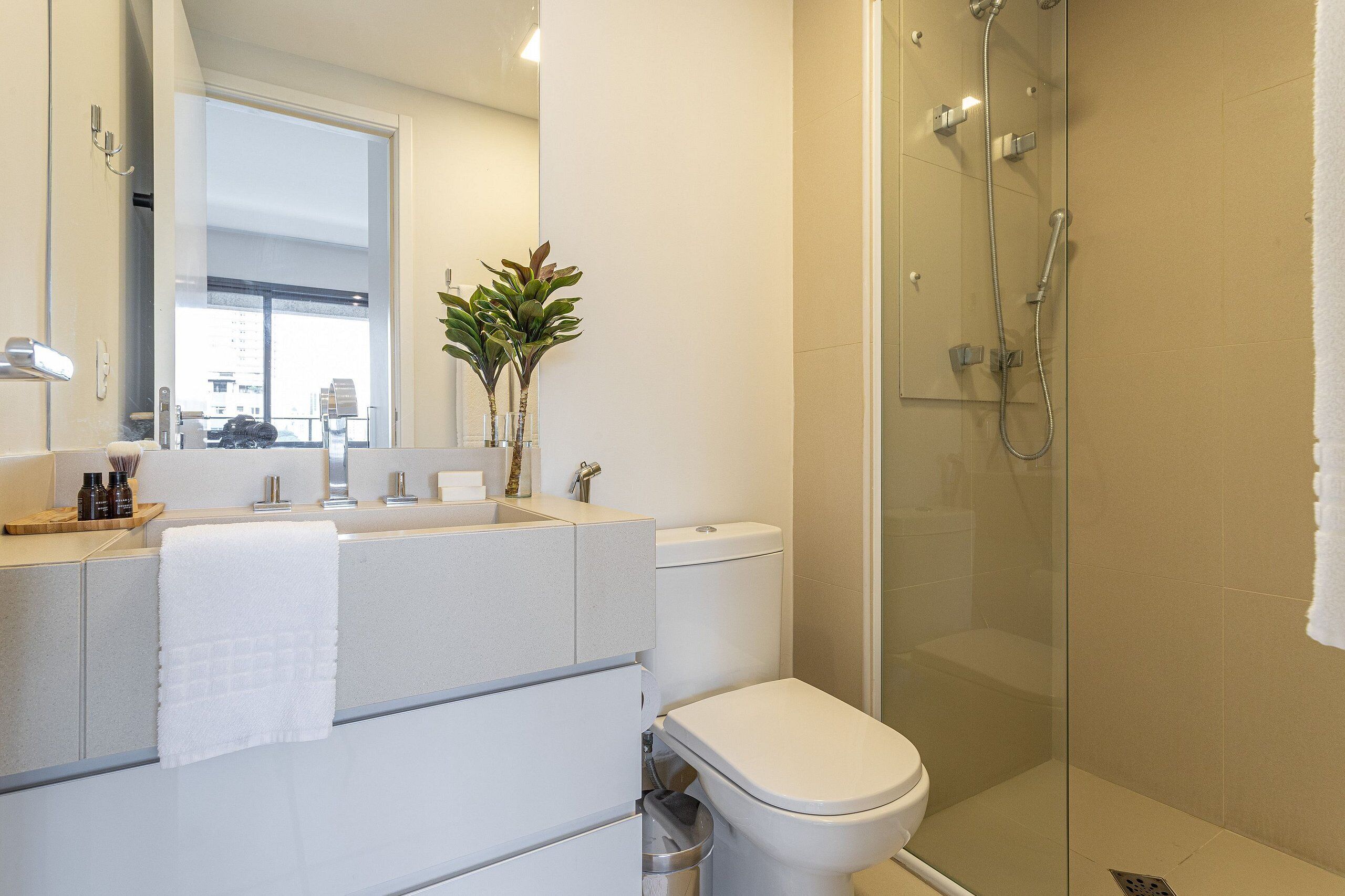 A modern bathroom with a glass-enclosed shower, a white toilet, and a vanity with a mirror and towel.