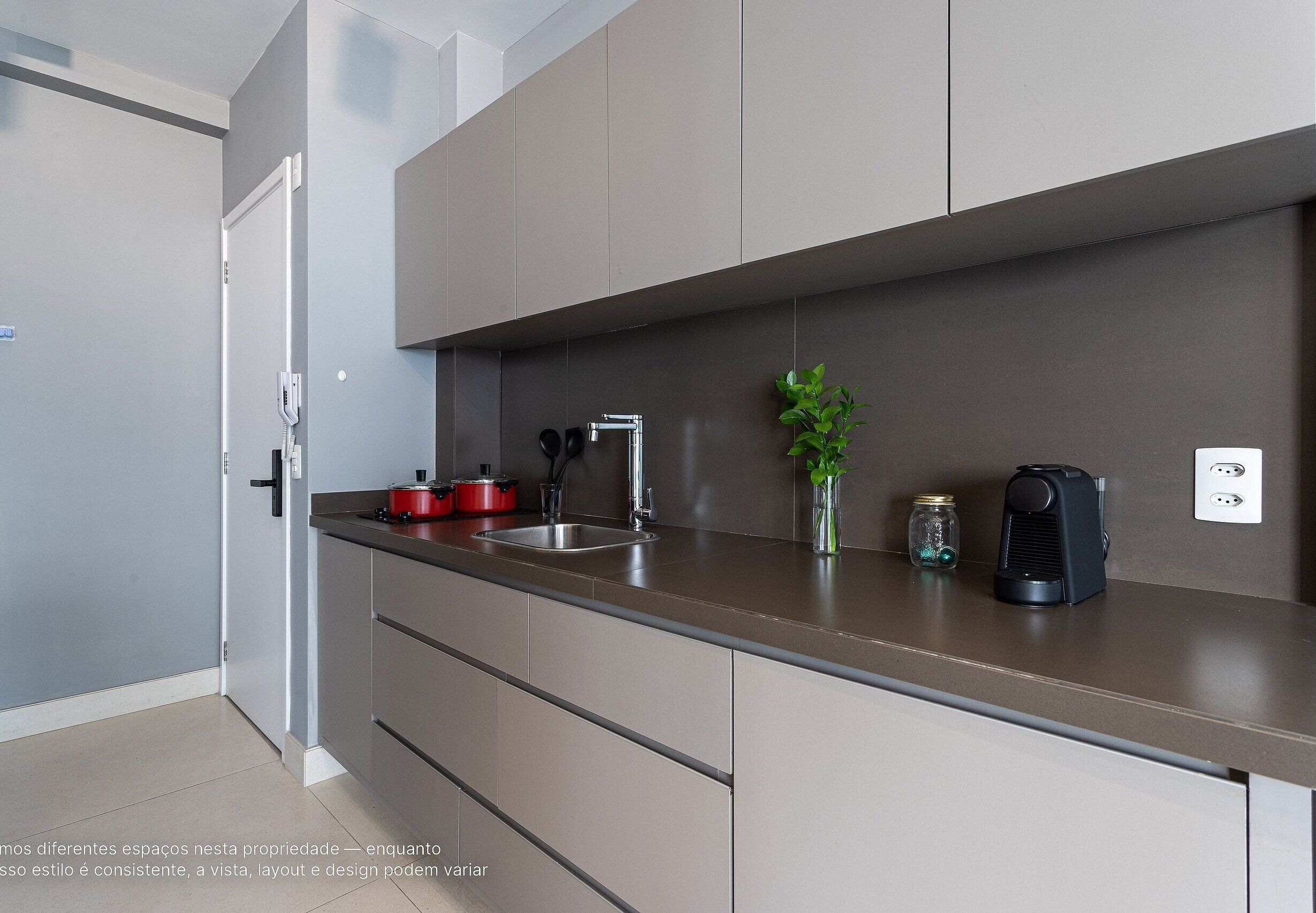 A modern kitchen with grey cabinets, a stainless steel sink, and a black coffee maker.