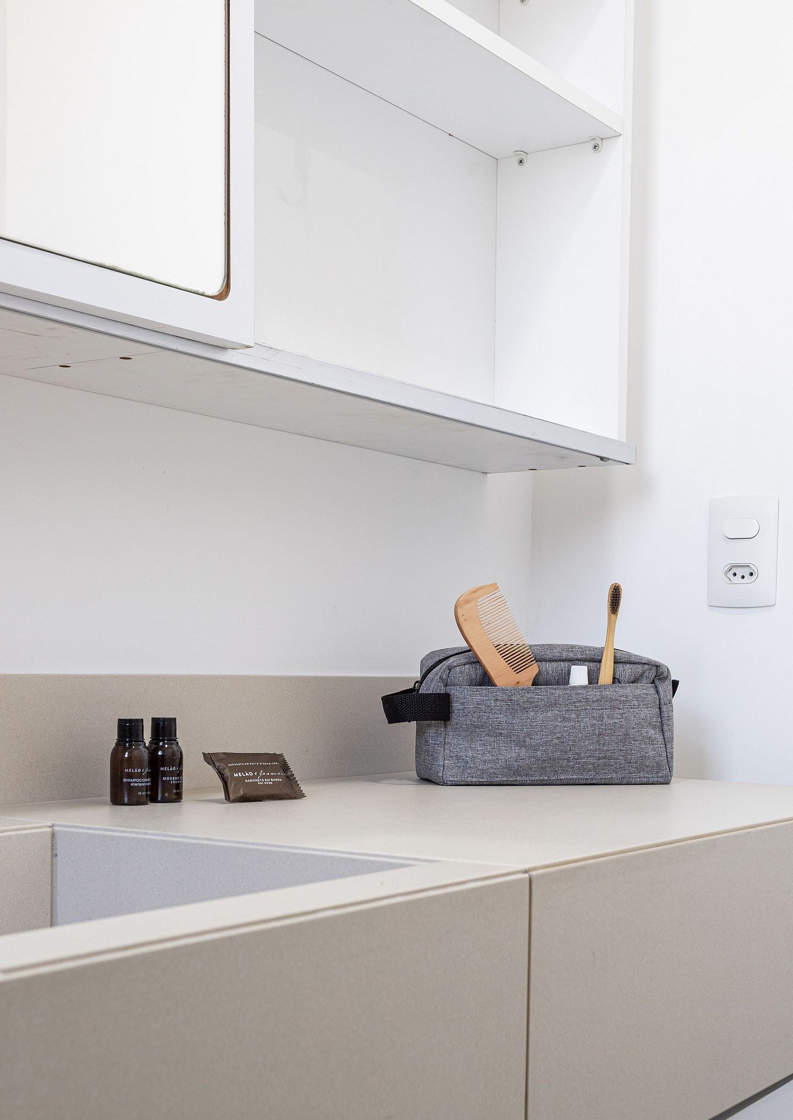 A bathroom with a white countertop, a grey toiletry bag with a comb and toothbrush, and two bottles of hair product.