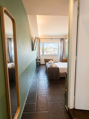 A hotel room with a bed, a small table, a chair, a mirror, and a window with a view.