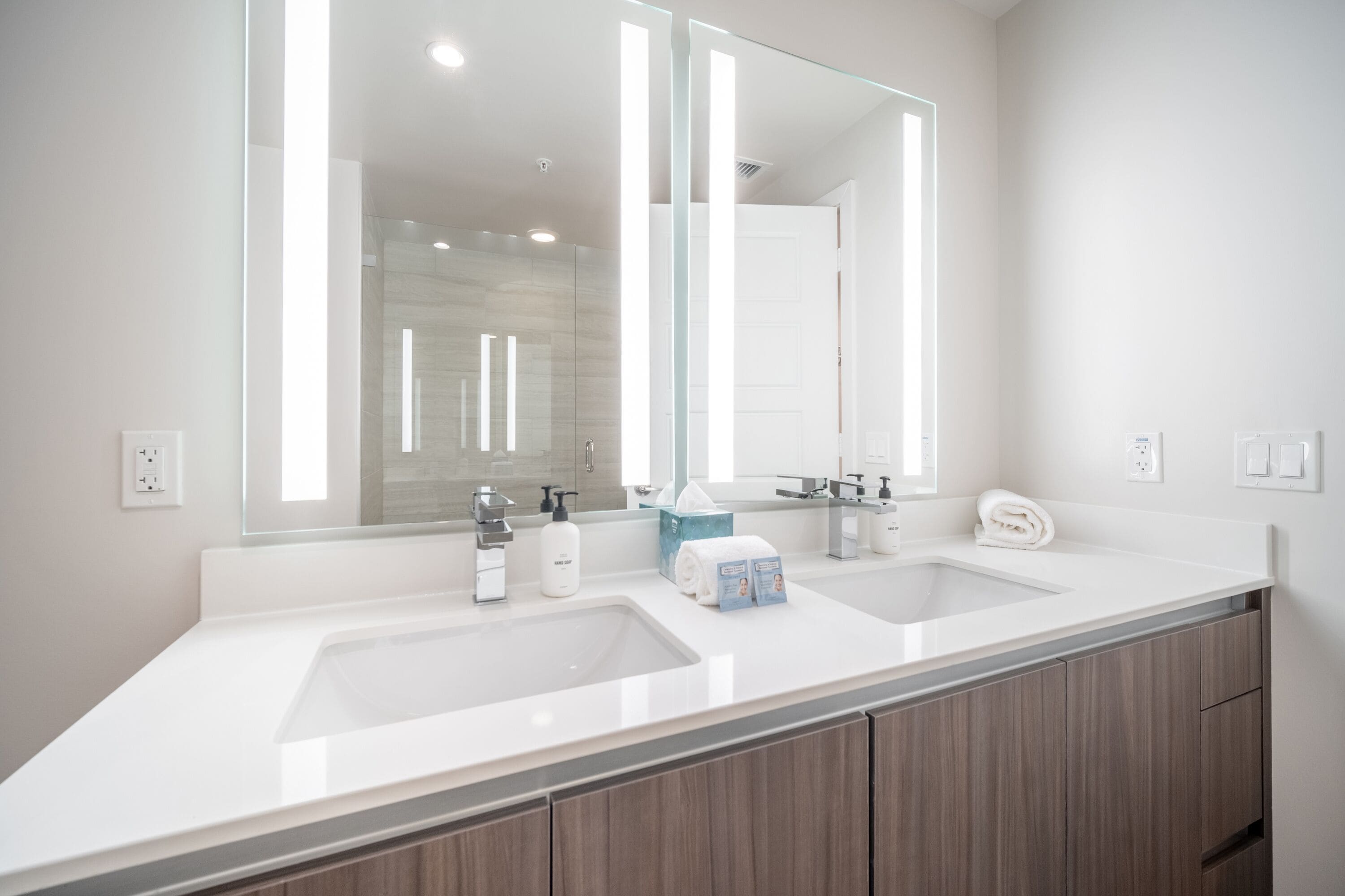 A modern bathroom with two sinks, a large mirror, and wooden cabinets.