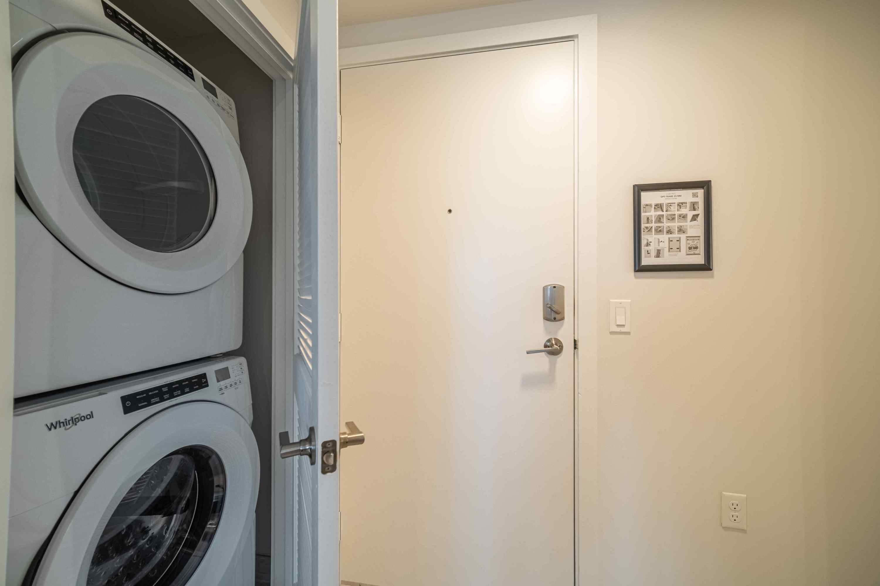A laundry room with stacked Whirlpool washers and dryers, a closed door, and a framed informational poster on the wall.