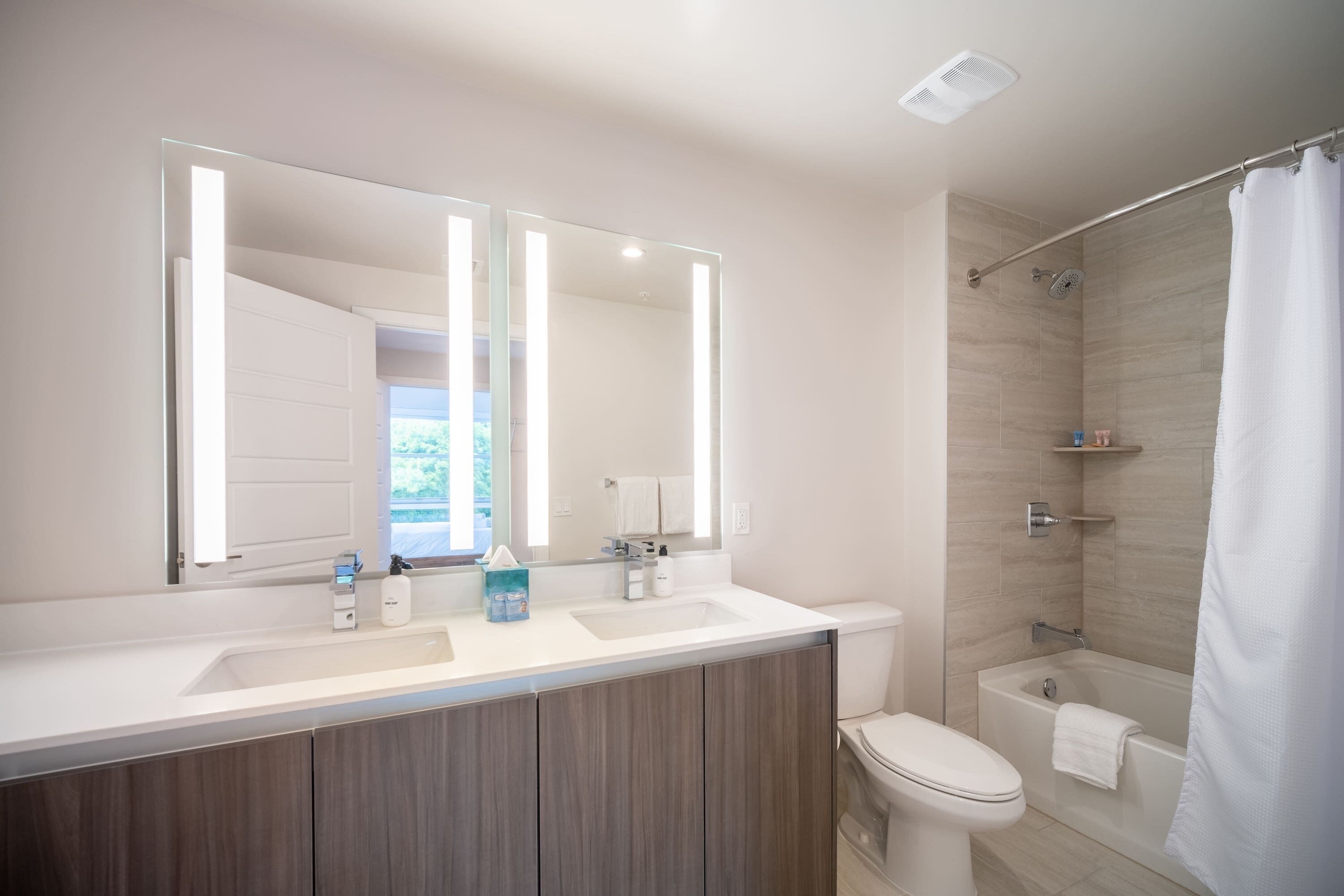 A modern bathroom with a double sink vanity, a toilet, a shower, and a large mirror.