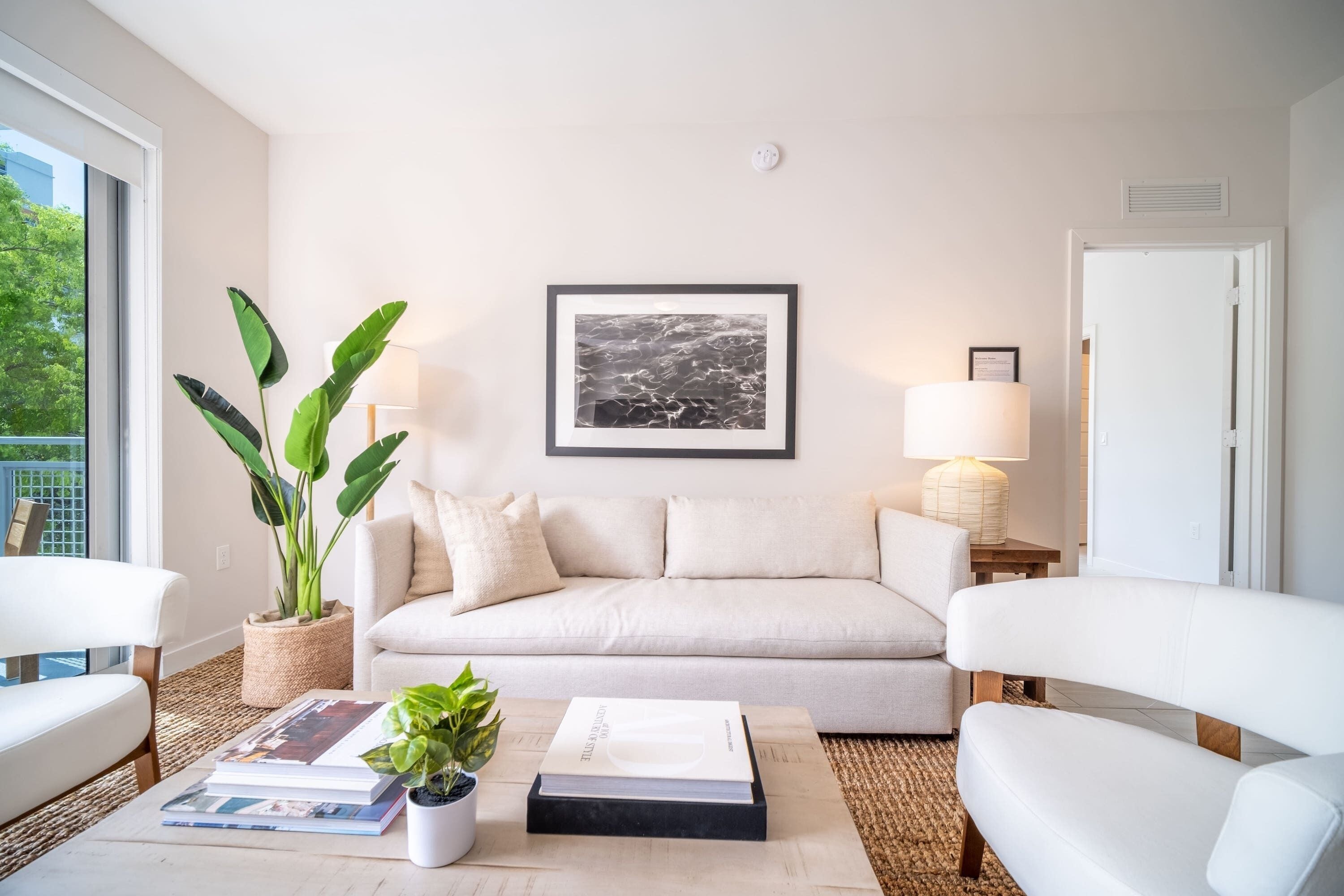 Un salon moderne comprenant un canapé, deux fauteuils, une table basse avec des livres et une plante, un tableau encadré au mur et une lampe.