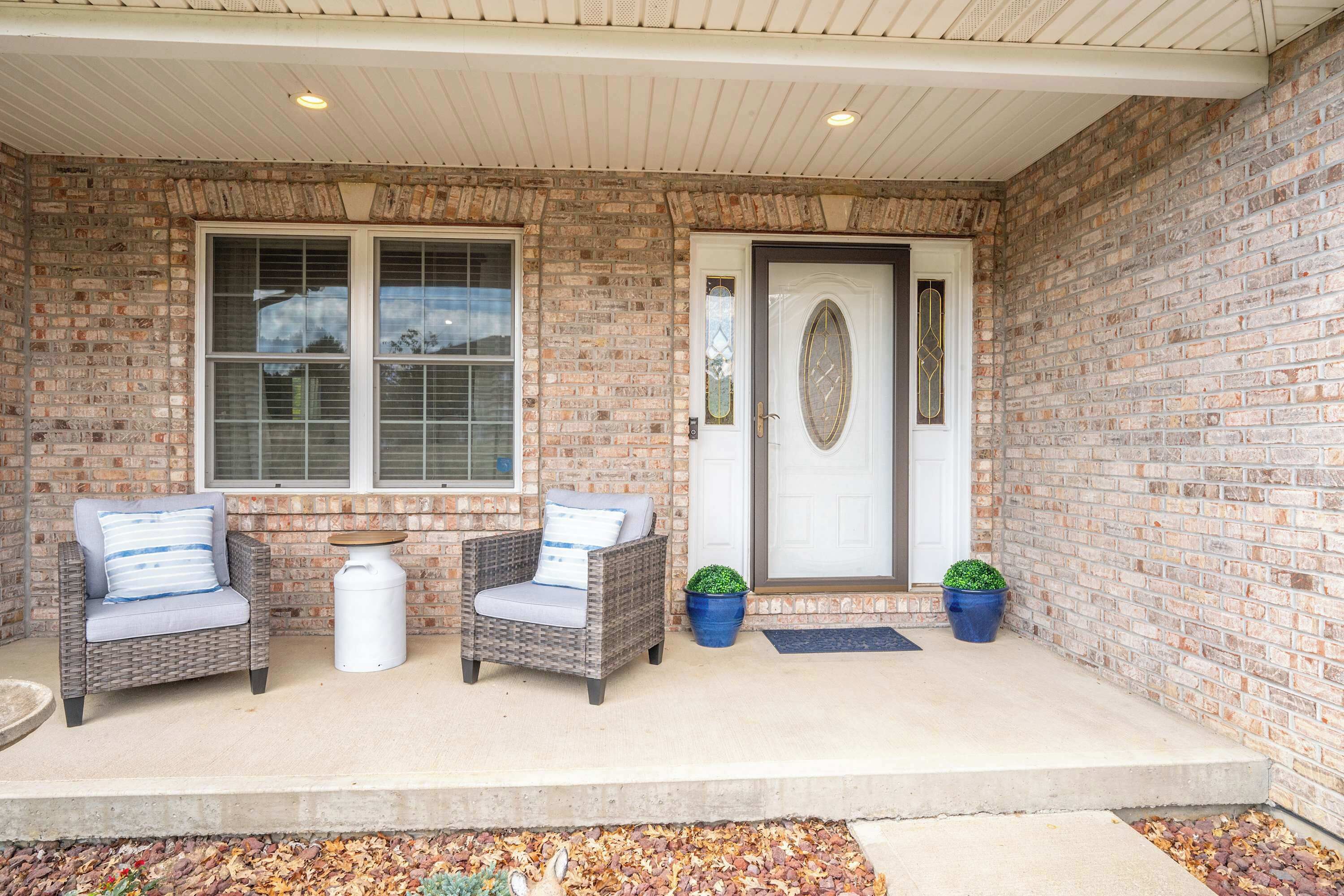 A covered porch with two wicker chairs, a small table, and two potted plants.