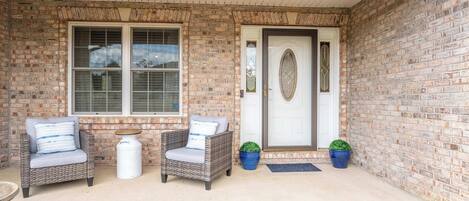 A covered porch with two wicker chairs, a small table, and two potted plants.