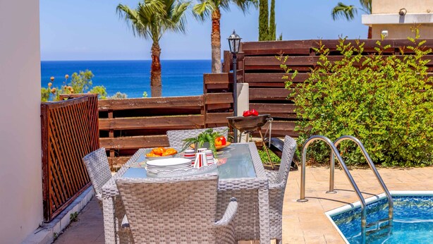 A patio with a pool, wicker furniture, and a view of the sea. - Villa Korona - Three Bedroom Villa, Sleeps 6 (Neo Chorio)