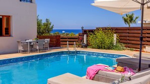 A swimming pool with lounge chairs and a table, a wooden fence, and a view of the sea. - Villa Korona - Three Bedroom Villa, Sleeps 6 (Neo Chorio)