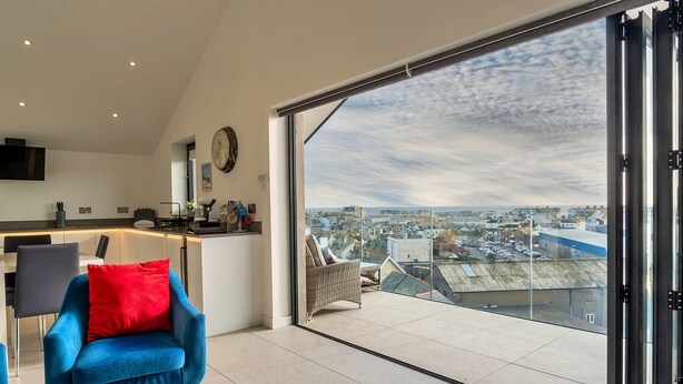 A modern living room with a large sliding glass door leading to a balcony with a city view. - Anchor View (Teignmouth)
