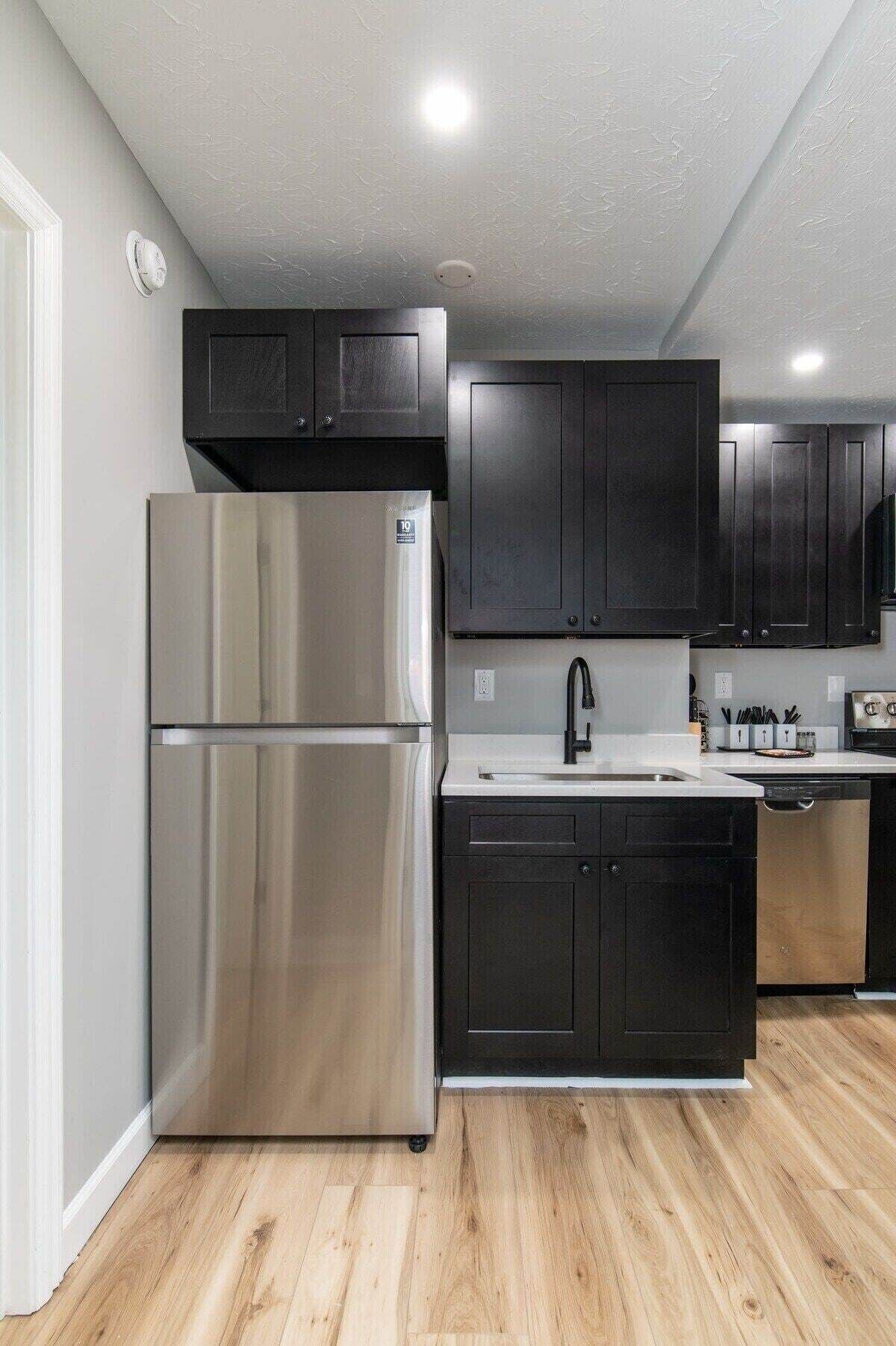 Una cocina moderna con electrodomésticos de acero inoxidable, armarios oscuros y piso de madera.