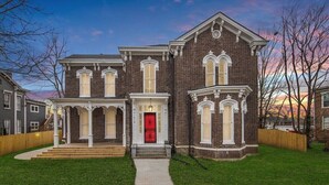A two-story brick house with a red door, white trim, and a front porch.