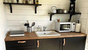 A compact kitchen with a wooden countertop, a white sink, a microwave, and black cabinets with brass handles.