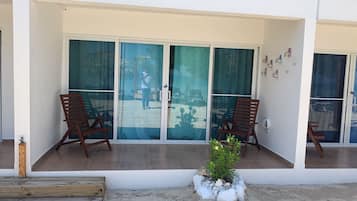 A balcony with two wooden chairs, a small potted plant, and a glass door with a view of a sandy area.