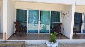 A balcony with two wooden chairs, a small potted plant, and a glass door with a view of a sandy area.