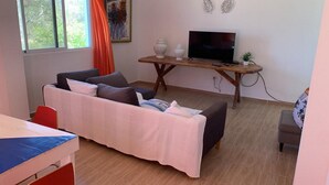 Een woonkamer met een bank, een televisie op een houten dressoir en een bijzettafeltje met decoratieve objecten.