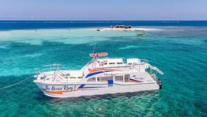 Een boot genaamd "The Ocean King" afgemeerd in helder turquoise water, met een strand en andere boten op de achtergrond.