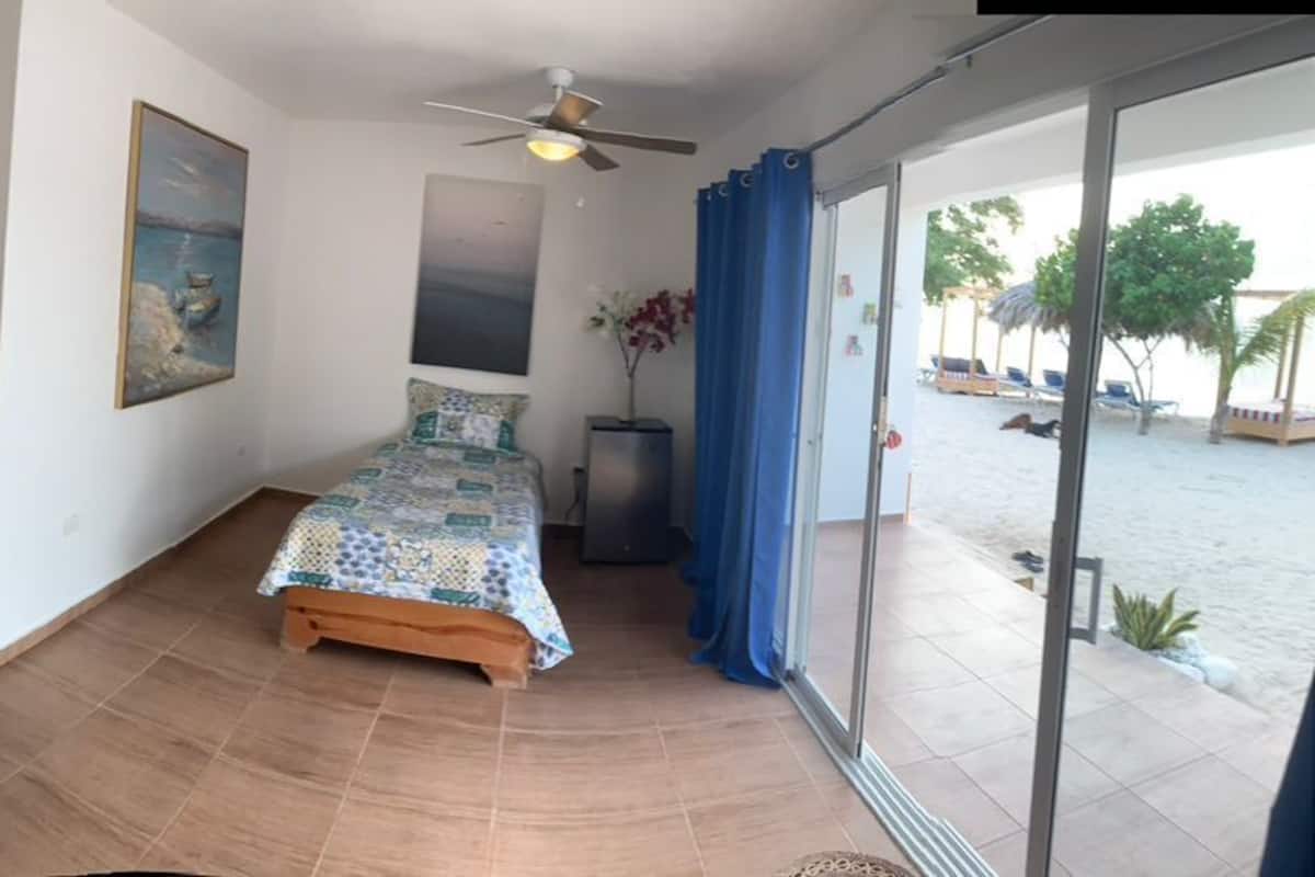 A bedroom with two beds, a ceiling fan, and a view of the beach through the glass door.
